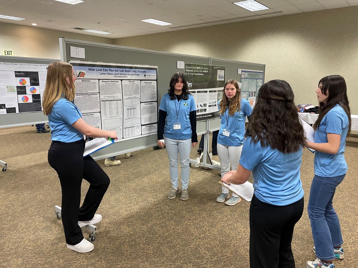 three students stand with their research poster while two others ask them questions in a peer review session