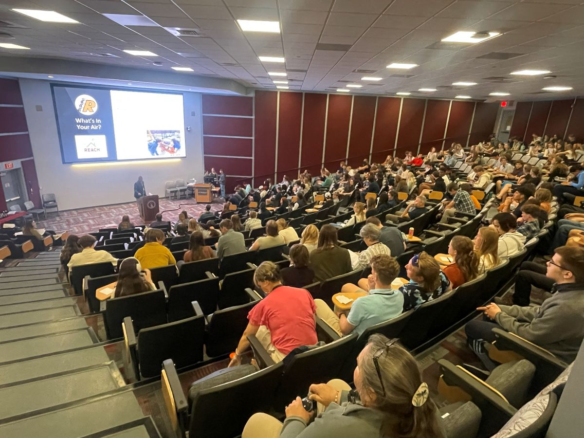 a lecture hall is filled with high school students watching a presentation by 3 Ronan Middle School students as they project slides on a large screen